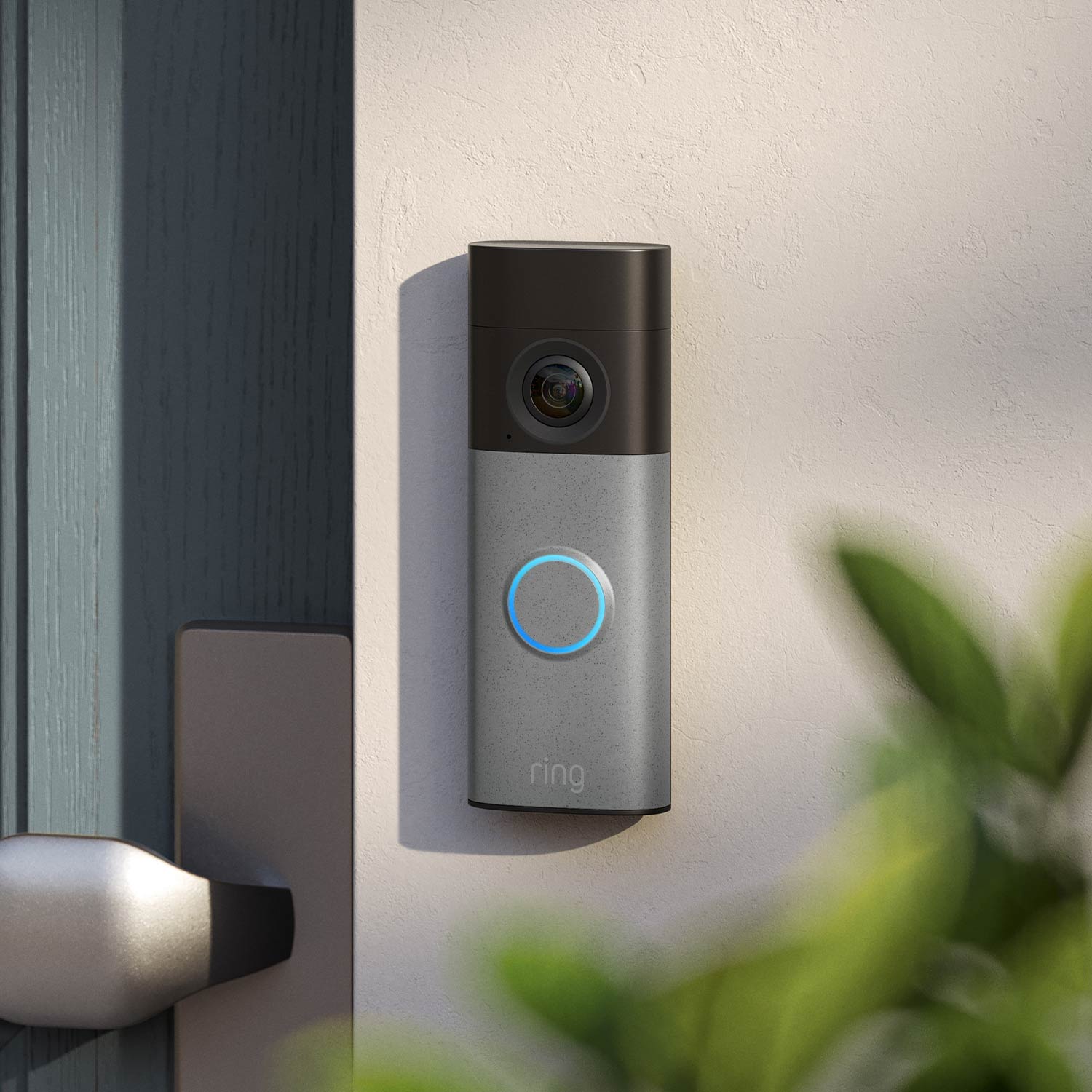 Ring smart doorbell with camera mounted on an exterior wall near the door, blue ring light illuminated