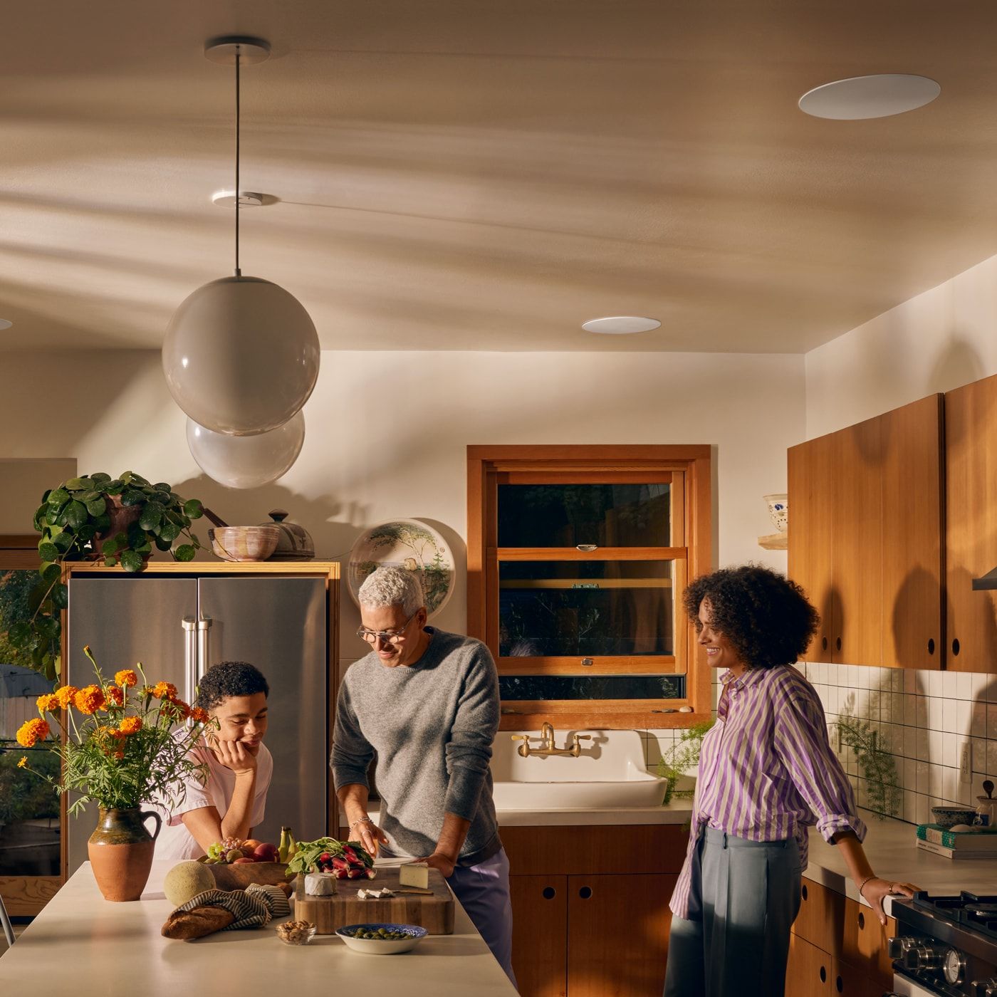 Three people prepare food together at a kitchen island in a warm, well-lit modern kitchen.