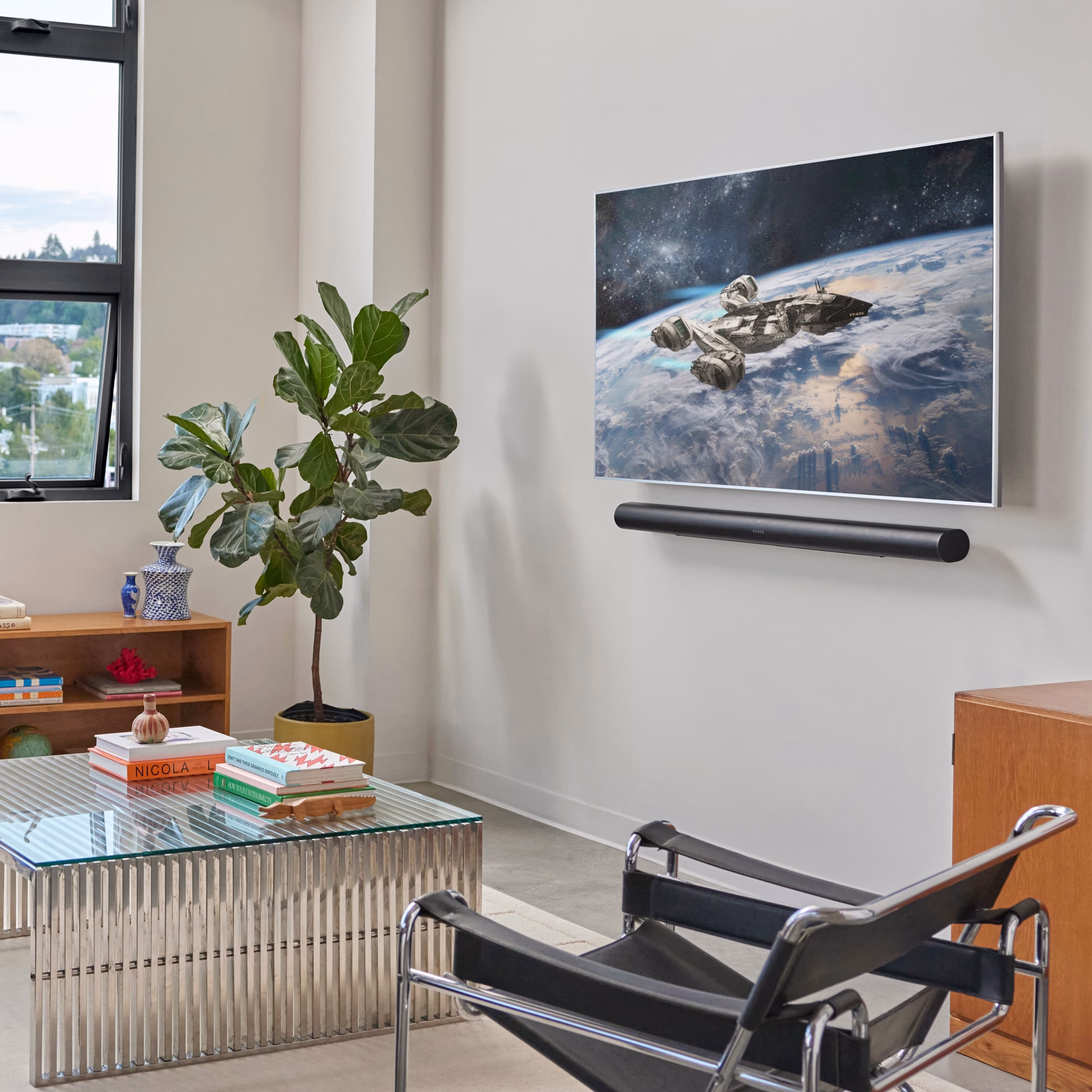 Living room with a wall-mounted screen showing an Earth-from-space image; nearby are a leafy plant and a glass coffee table with books.